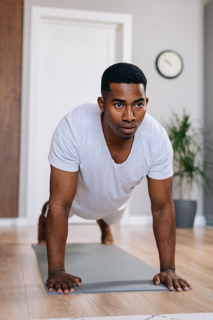 Vue rapprochée de l'homme afro-américain concentré faisant des pompes sur le sol de la chambre domestique en détournant les yeux