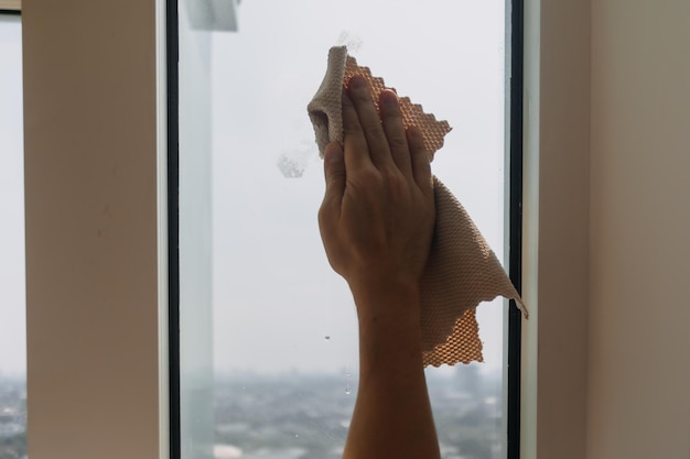 Vue rapprochée d'un homme essuyant et nettoyant à la main le verre de la fenêtre dans l'appartement de la chambre. Gardez le verre propre et étincelant.