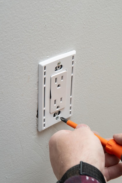 Vue rapprochée d'un homme installant une prise électrique dans le mur d'une pièce de la maison.