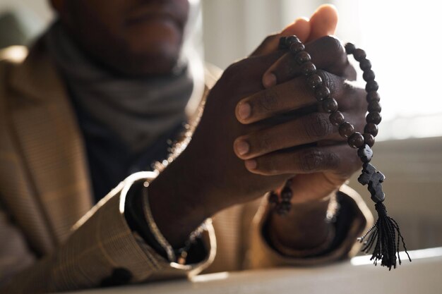 Photo vue rapprochée d'un homme noir priant dans les mains de l'église tenant un chapelet