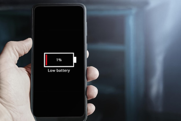 Photo vue rapprochée d'un homme tenant un smartphone à la main avec une icône de batterie faible sur l'écran indiquant que le niveau de batterie est à un pour cent épuisement de la batterie sur le téléphone portable