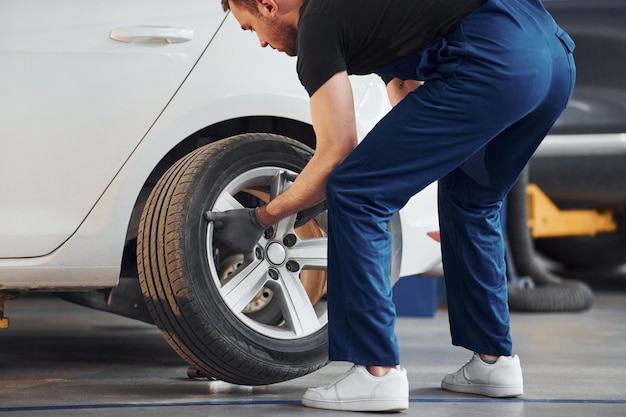 Vue rapprochée de l'homme en uniforme de travail avec roue de voiture à l'intérieur Conception du service automobile