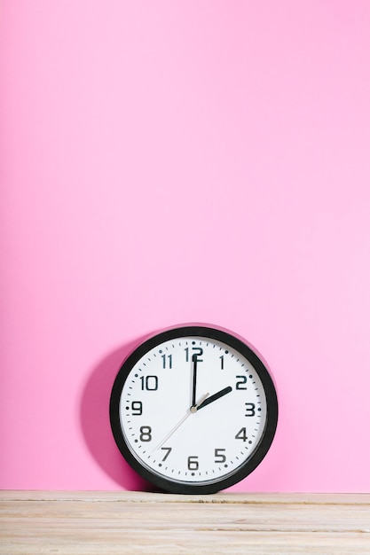 Photo vue rapprochée de l'horloge sur une table en bois contre un mur rose