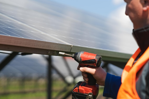 Vue rapprochée de l'ingénieur qui serre les boulons des panneaux solaires sur une base métallique avec une perceuse électrique