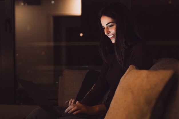 Vue rapprochée d'une jeune femme heureuse et joyeuse souriante et utilisant un ordinateur portable à la maison assise sur le canapé