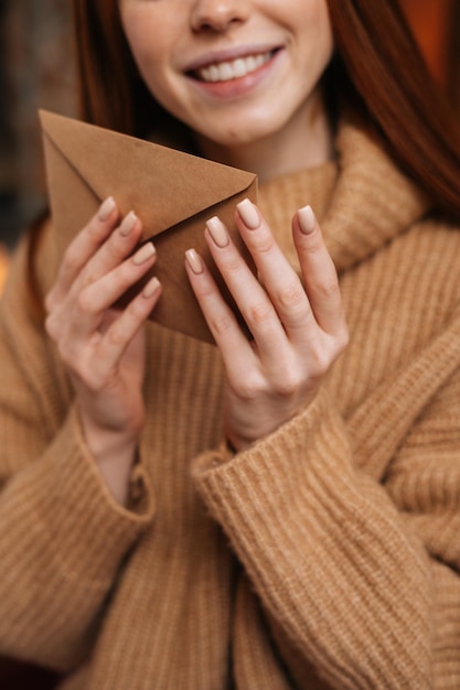 Vue rapprochée d'une jeune femme souriante rousse tenant dans les mains une enveloppe en papier devant elle