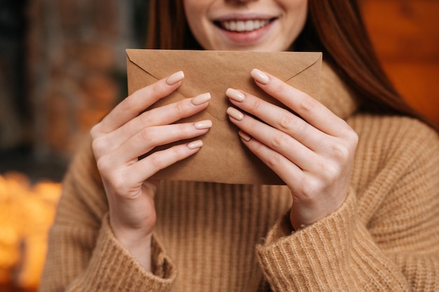 Vue rapprochée d'une jeune femme souriante rousse tenant dans les mains une enveloppe en papier devant elle