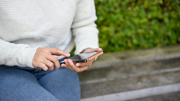 Vue rapprochée d'une jeune femme utilisant un smartphone dans le parc en position assise
