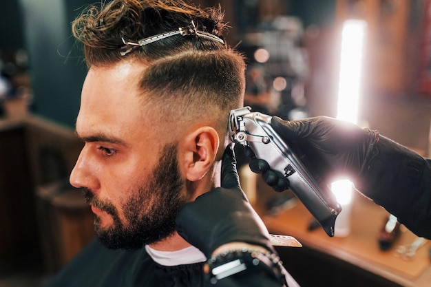 Photo vue rapprochée d'un jeune homme barbu assis et se faisant couper les cheveux dans un salon de coiffure