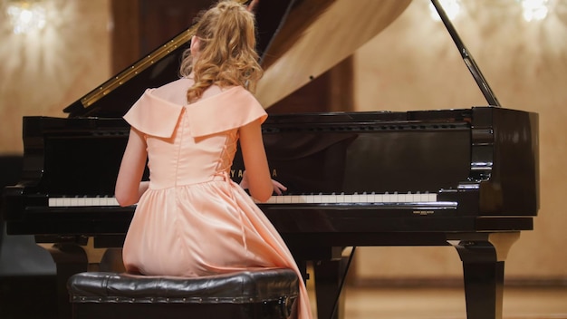 Vue rapprochée d'une jolie adolescente joue du piano dans la salle de concert sur scène