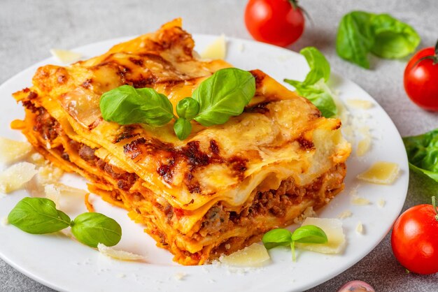 Vue rapprochée de la lasagne à la viande avec des tomates de basilic frais et du fromage parmesan dans une assiette de cuisine italienne