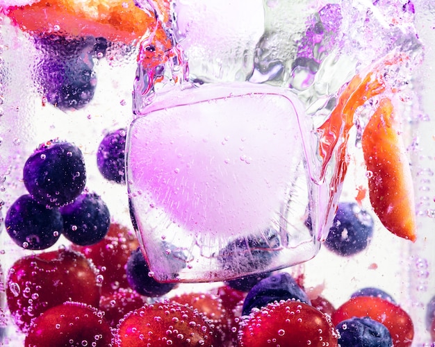 Vue rapprochée de la limonade froide et fraîche avec des baies lumineuses et des glaçons à la lumière du néon. Texture de la boisson d'été rafraîchissante avec des bulles macro sur verre. Fizzing ou flottant jusqu'au sommet de la surface.