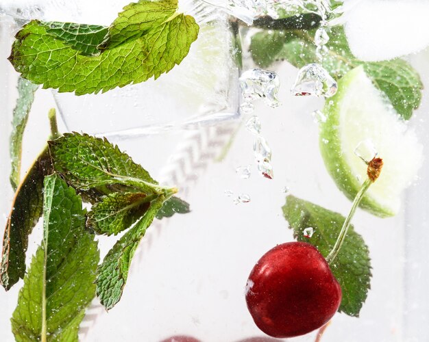 Vue rapprochée de la limonade froide et fraîche avec des cerises, des feuilles de menthe et des glaçons. Texture de la boisson d'été rafraîchissante avec des bulles macro sur verre. Fizzing ou flottant jusqu'au sommet de la surface.