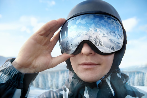 Vue rapprochée des lunettes de ski d'un homme avec le reflet de montagnes enneigées