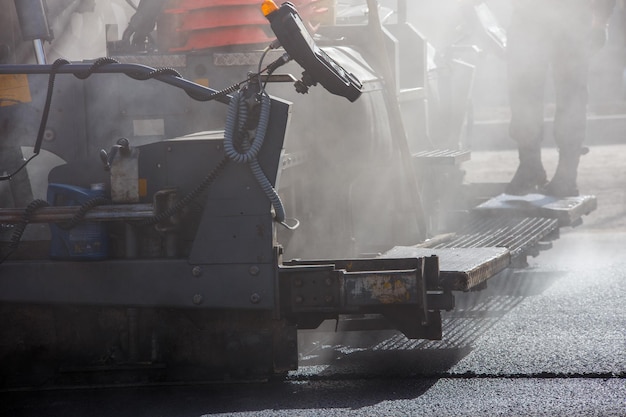 Vue rapprochée de la machine à paver d'asphaltage pendant les travaux de réparation de la rue à la lumière du jour avec de la fumée et de la vapeur dans l'air