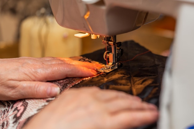 Une vue rapprochée de la main du processus de couture de la vieille femme à l'aide de la technique de mise au point sélective de la machine à coudre