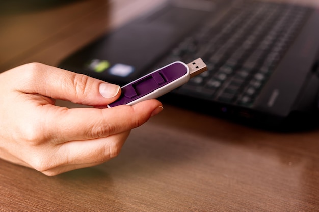 Vue rapprochée de la main d'une femme avec une clé USB près de l'ordinateur portable