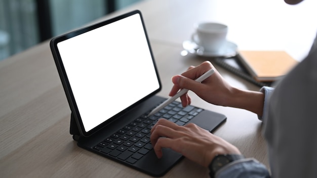 Vue rapprochée d'une main de femme tenant un stylet et travaillant sur une tablette informatique au bureau.