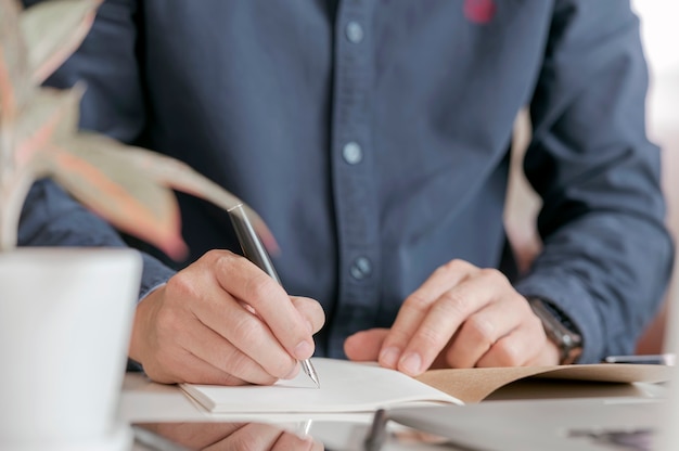 Vue rapprochée de la main de l'homme écrit sur un ordinateur portable avec un stylo-plume.