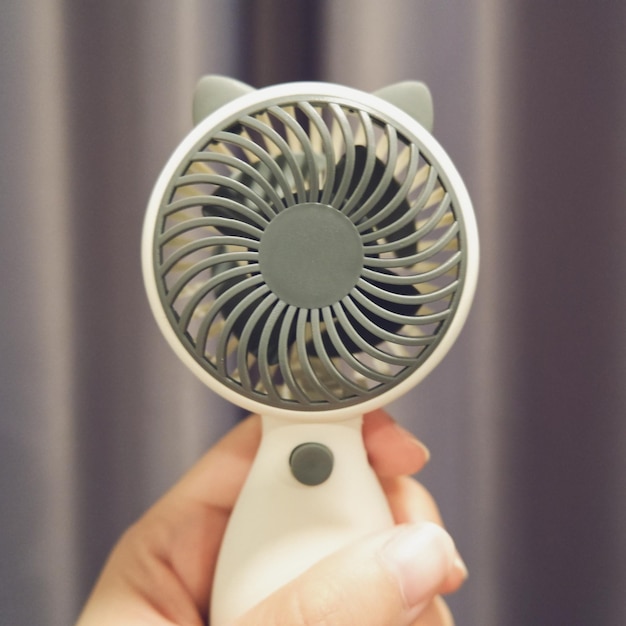 Vue rapprochée d'une main humaine tenant un ventilateur portable blanc