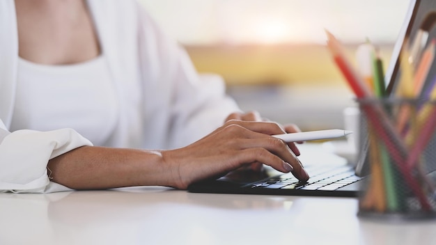 Vue rapprochée de la main d'une jeune femme designer tenant un stylet et travaillant sur une tablette informatique.