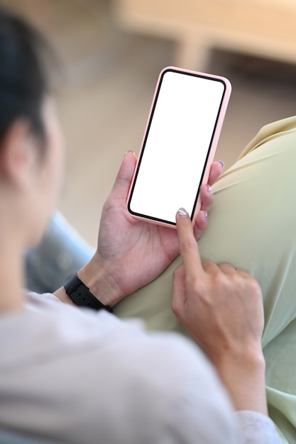 Vue rapprochée de la main de la jeune femme pointant sur l'écran de la maquette du téléphone intelligent avec un écran vide alors qu'il était assis sur le canapé.