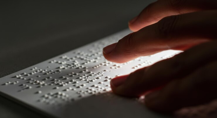 Photo vue rapprochée d'une main lisant un texte en braille gravé sur du papier