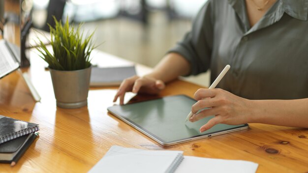 Vue rapprochée des mains féminines à l'aide d'une tablette numérique sur un espace de travail en bois avec des fournitures de bureau