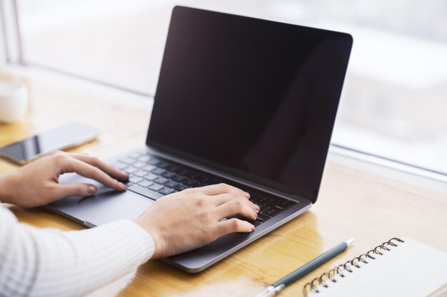 Une vue rapprochée de mains féminines tapant sur un clavier d'ordinateur portable de pointe avec un bureau flou derrière