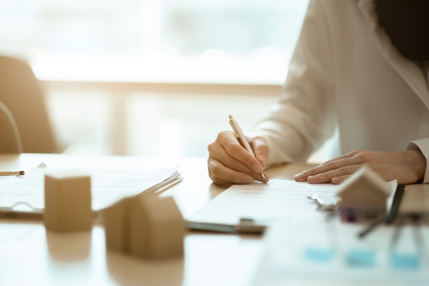 Vue rapprochée des mains d'une femme d'affaires signant des documents de location de maison et avoir les clés d'un appartement sur la paperasse.