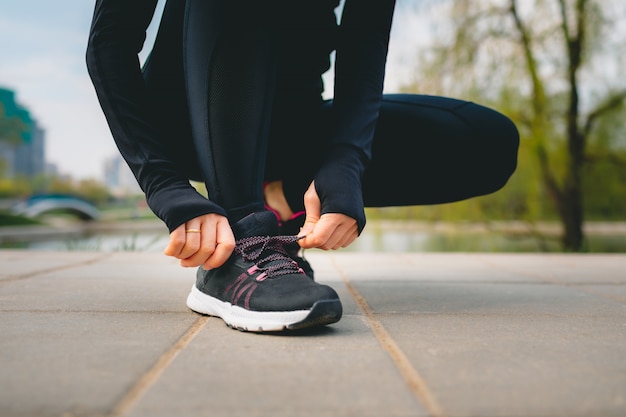 Vue rapprochée des mains de la femme en costume de sport attachant les lacets sur ses baskets de sport lors de l'exécution dans le parc