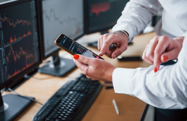 Vue rapprochée des mains des gens avec un téléphone et des graphiques dessus. Les agents de change ont un travail.