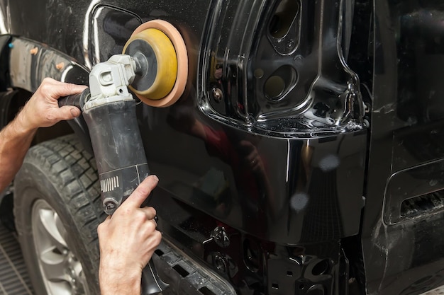 Vue rapprochée sur les mains d'un travailleur masculin qui détient un outil pour polir l'aile d'une voiture tout en travaillant dans un atelier de détail de véhicules Industrie des services automobiles