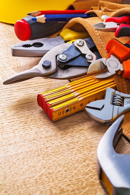 Vue rapprochée marteau ruban à mesurer pinces pinces clé cutter crayon dans la ceinture à outils sur planche de bois