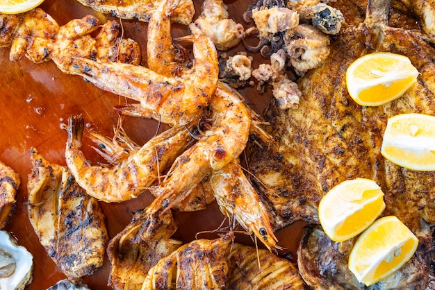 Photo vue rapprochée d'un mélange de fruits de mer grillés sur une assiette en bois, un plateau de charcuterie avec des crevettes, des huîtres et des poissons