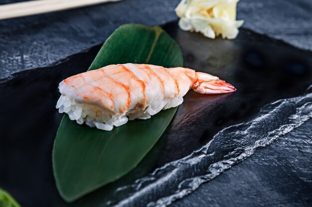 Vue rapprochée sur Nigiri servi avec des crevettes sur une plaque sombre sur une surface sombre