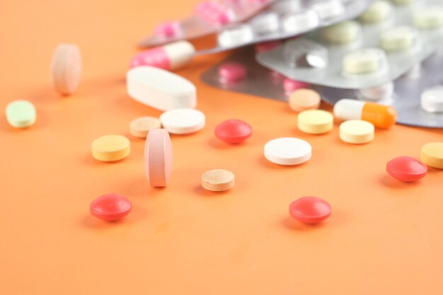 Vue rapprochée de nombreuses pilules et capsules colorées sur un fond orange