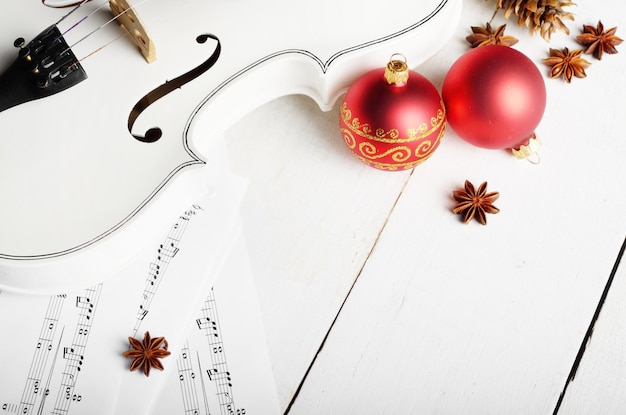 Vue rapprochée d'une note de musique de violon et de boules rouges de décoration de Noël sur une table en bois blanche