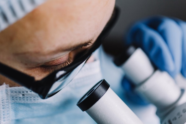 Vue rapprochée de l'œil du scientifique dans des verres regardant un microscope