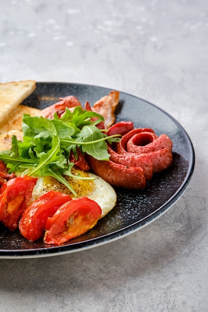 Vue rapprochée des œufs au plat avec des saucisses, du bacon, des tomates et des haricots sur une assiette avec des toasts