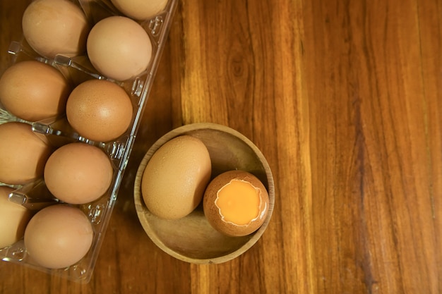 Vue rapprochée des œufs de poule crus dans une boîte à œufs sur fond de bois jaune.