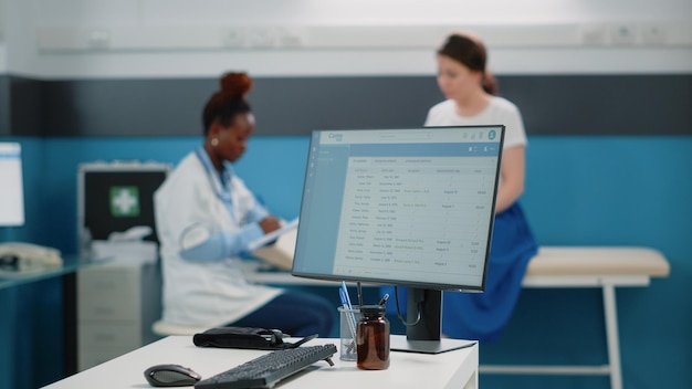 Photo vue rapprochée de l'ordinateur avec le médecin et le patient en arrière-plan