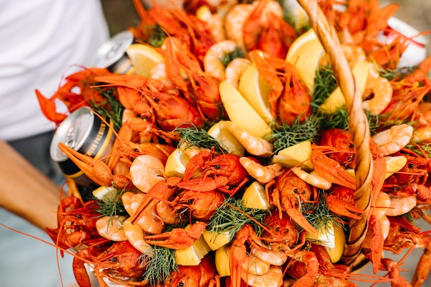 Vue rapprochée sur un panier festif rempli d'écrevisses fraîches et savoureuses, de crevettes et de canettes de bière décorées de tranches de citron et de grappes d'aneth.