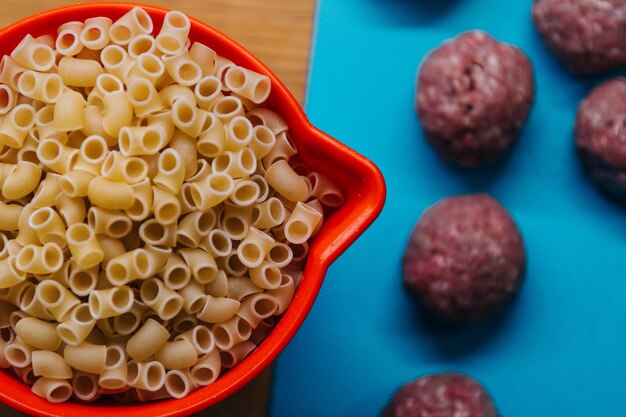 Photo vue rapprochée des pâtes crues dans la casserole par des boulettes de viande sur la table