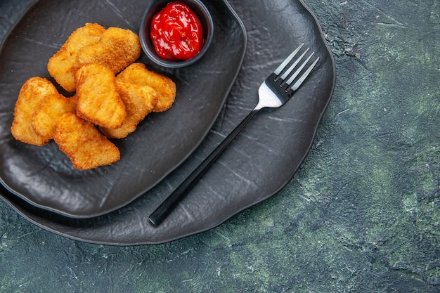 Vue rapprochée des pépites de poulet et de la fourchette de ketchup dans des assiettes noires sur une surface sombre