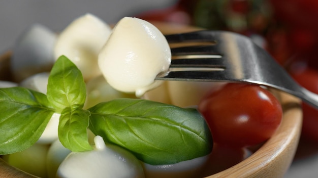 Photo vue rapprochée de la petite boule de fromage mozzarella fraîche des apulées sur un bol en bois et une feuille de basilic fraîche