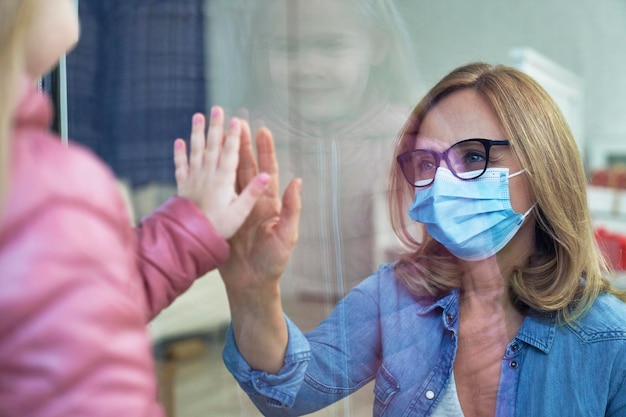 Vue rapprochée de la petite-fille rendant visite à sa grand-mère par la fenêtre