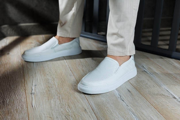 Vue rapprochée des pieds masculins dans des chaussures blanches décontractées Un jeune homme à la mode se tenant dans du cuir des mocassins blancs élégants dans des pantalons à la mode Chaussures d'homme d'été de saison Style de rue décontracté