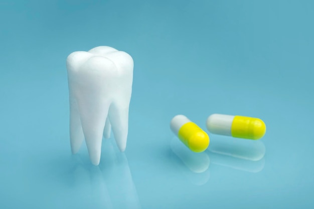 Vue rapprochée des pilules blanches jaunes et du modèle de dent sur fond bleu analgésiques remède pour les maux de dents