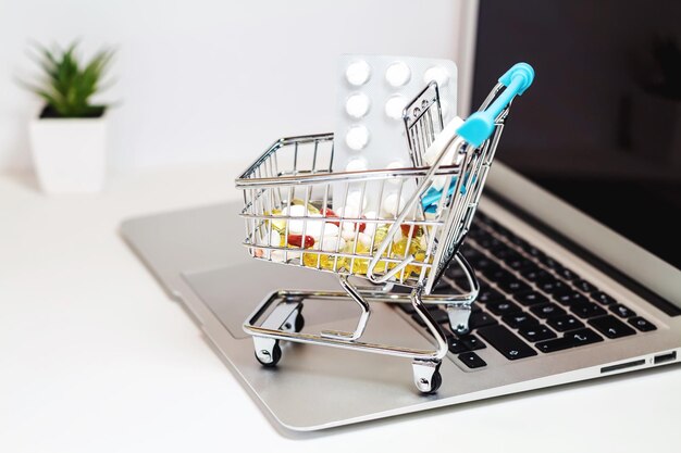 Vue rapprochée de pilules dans un petit panier d'achat sur un ordinateur portable à la table